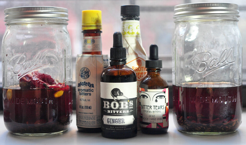 2 jars of homemade bitters with several bottles of store-bought bitters in the middle