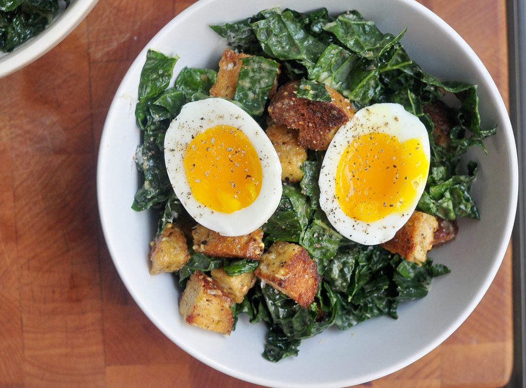 Kale Caesar salad with a two halves of a soft boiled egg on top