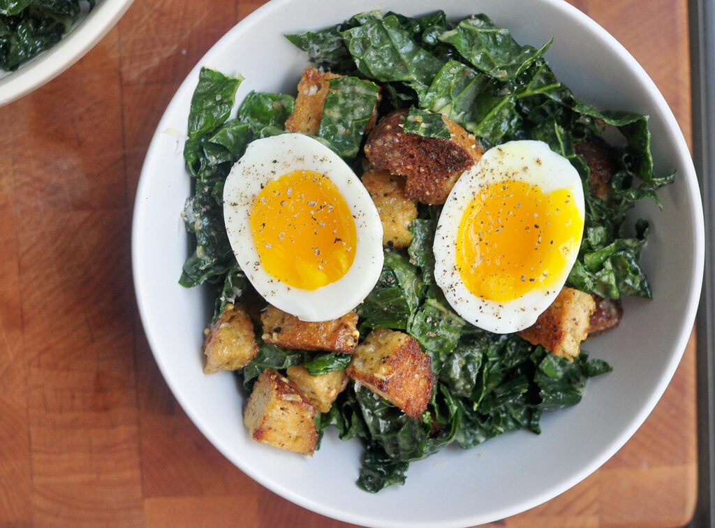 Kale Caesar salad with a two halves of a soft boiled egg on top