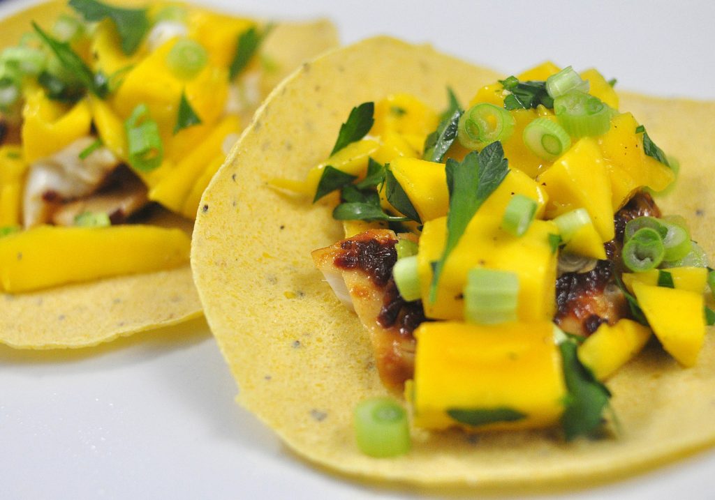 chipotle glazed tilapia tacos topped with mango and cilantro on a white plate