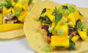 chipotle glazed tilapia tacos topped with mango and cilantro on a white plate