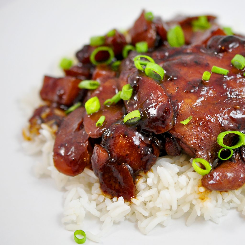 Chicken Adobo over a pile of white rice on a white background with scallions sprinkled on top
