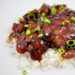 Chicken Adobo over a pile of white rice on a white background with scallions sprinkled on top