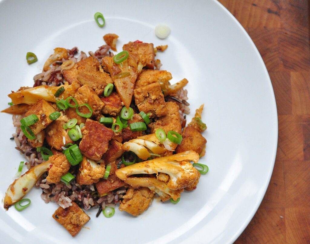 white plate with gochujang tofu and cauliflower on a bed of rice