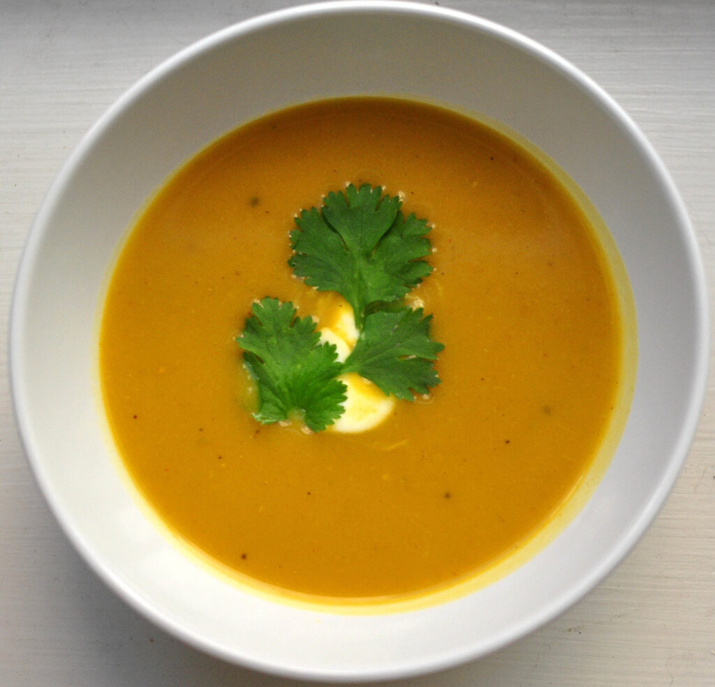 bowl of butternut squash soup with drizzle of sour cream and cilantro leaves