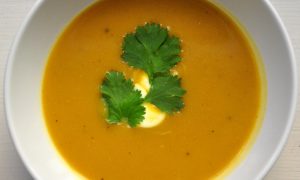 bowl of butternut squash soup with drizzle of sour cream and cilantro leaves