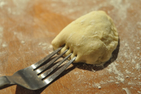 fork showing how to press the outside of the perogy together to make dumpling