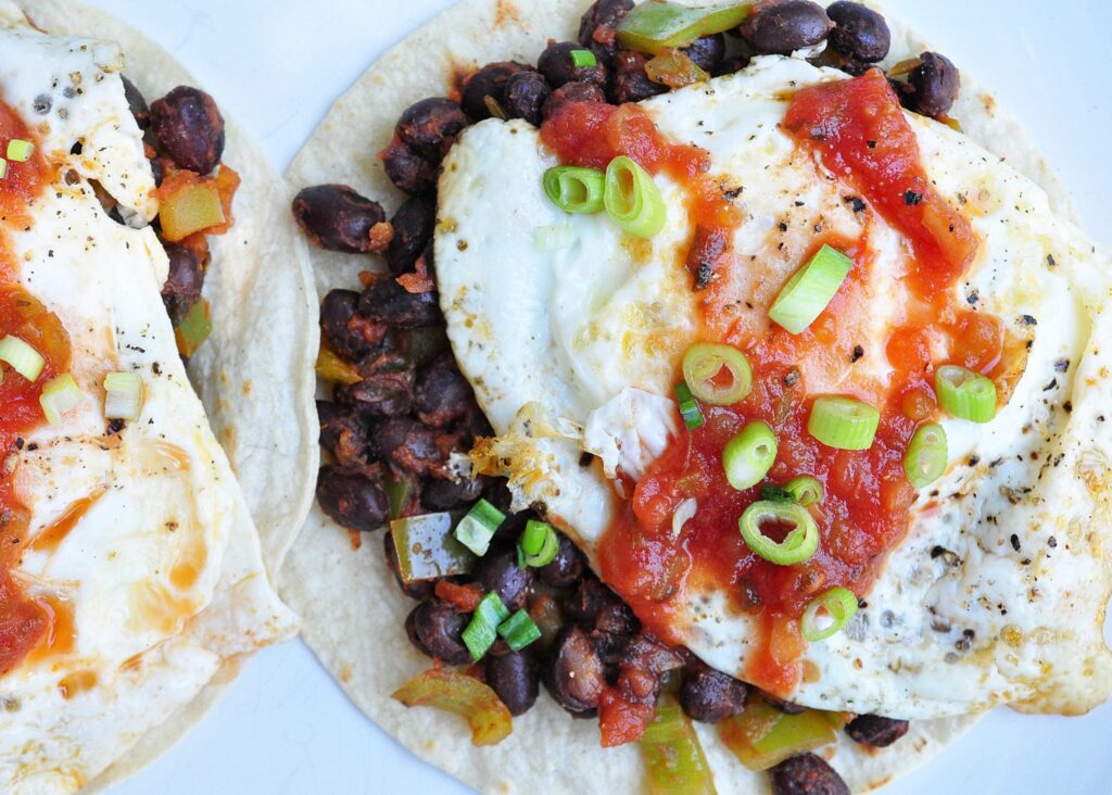 tortillas topped with beans, a fried egg, salsa and scallions