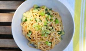 white bowl with sesame noodles topped with cucumbers and scallions