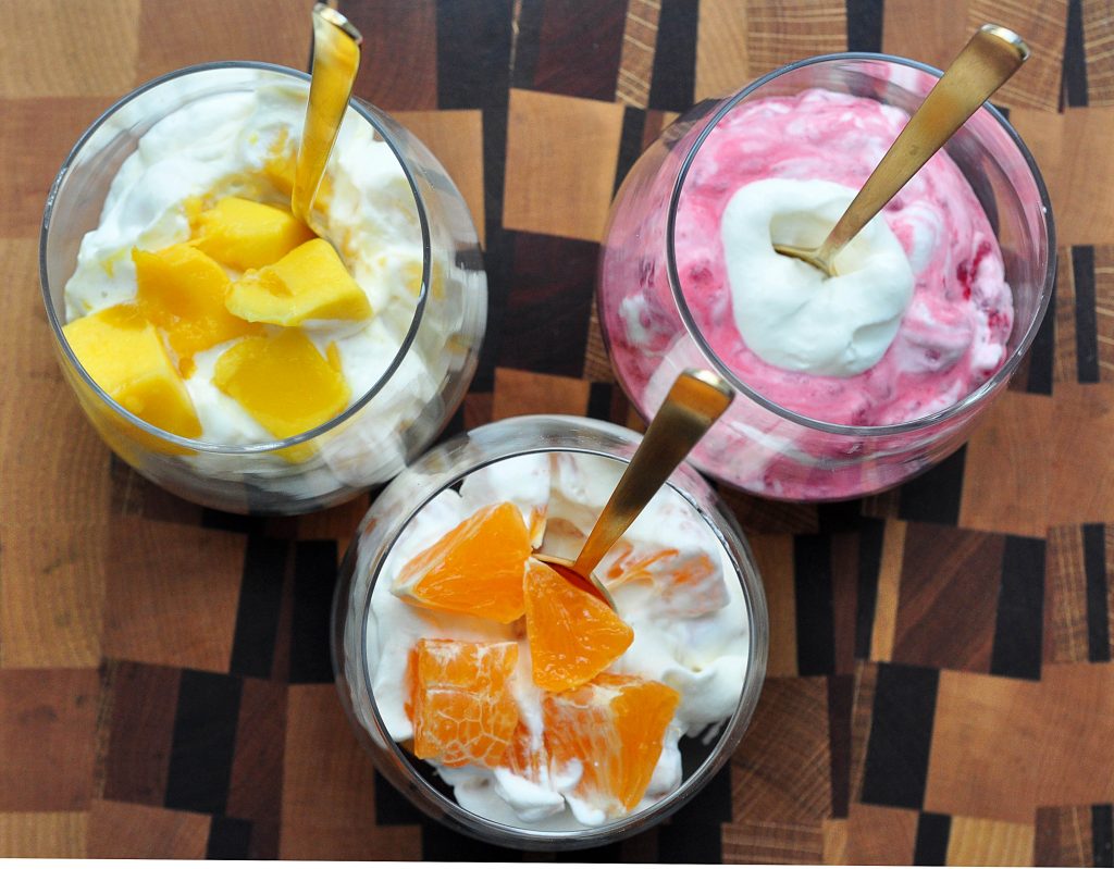 cups of whipped cream with mango, oranges and raspberries clustered on a board from above