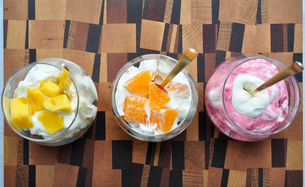 whipped cream with mango, oranges and raspberries in cups with gold spoons