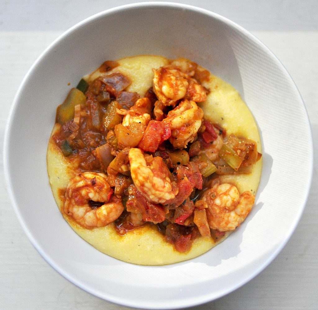 White bowl with shrimp and vegetables topping a layer of grits
