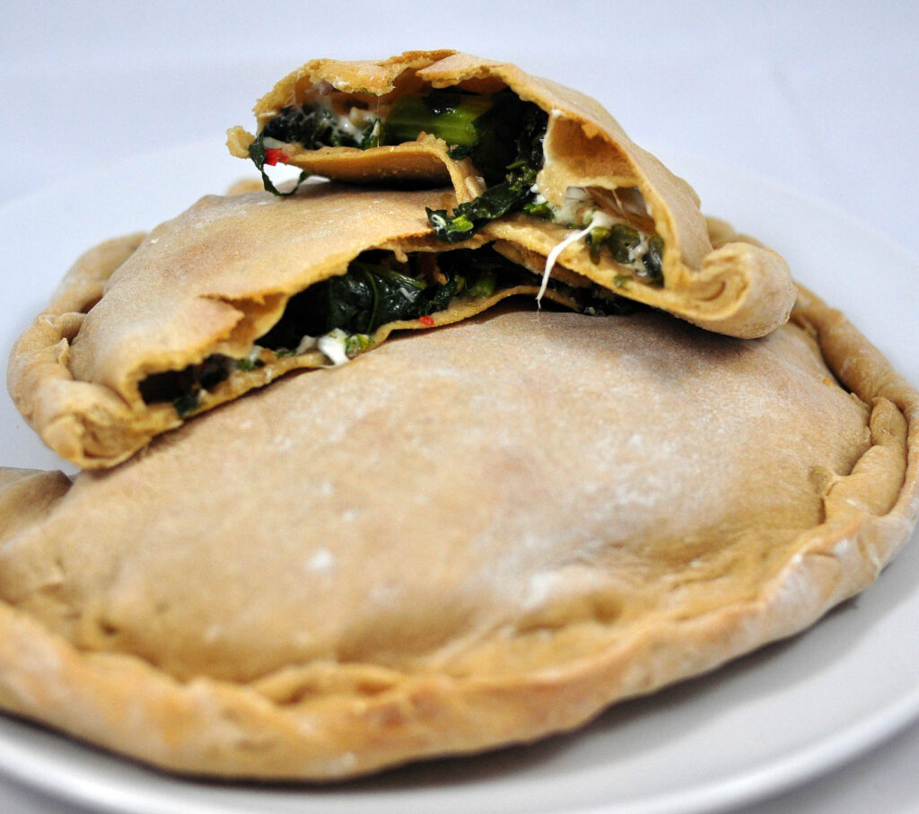 broccoli rabe calzone cut in half laying on top of another calzone