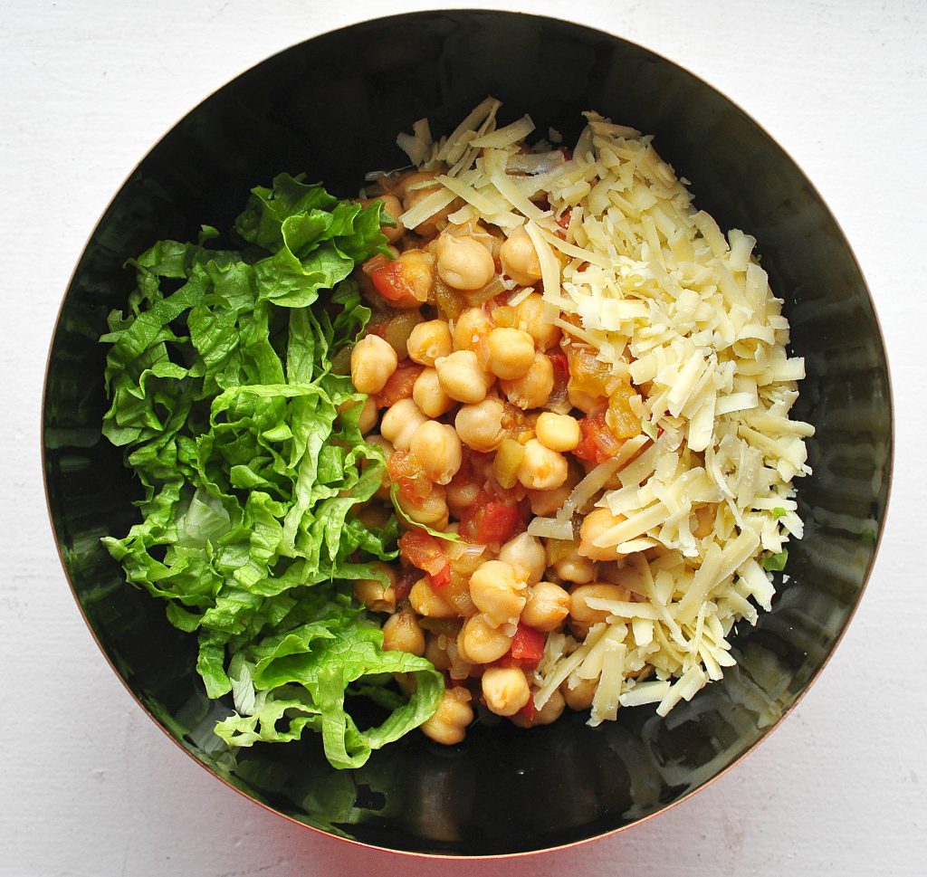 black bowl on white background full of chickpeas, cheese and lettuce taco bowl
