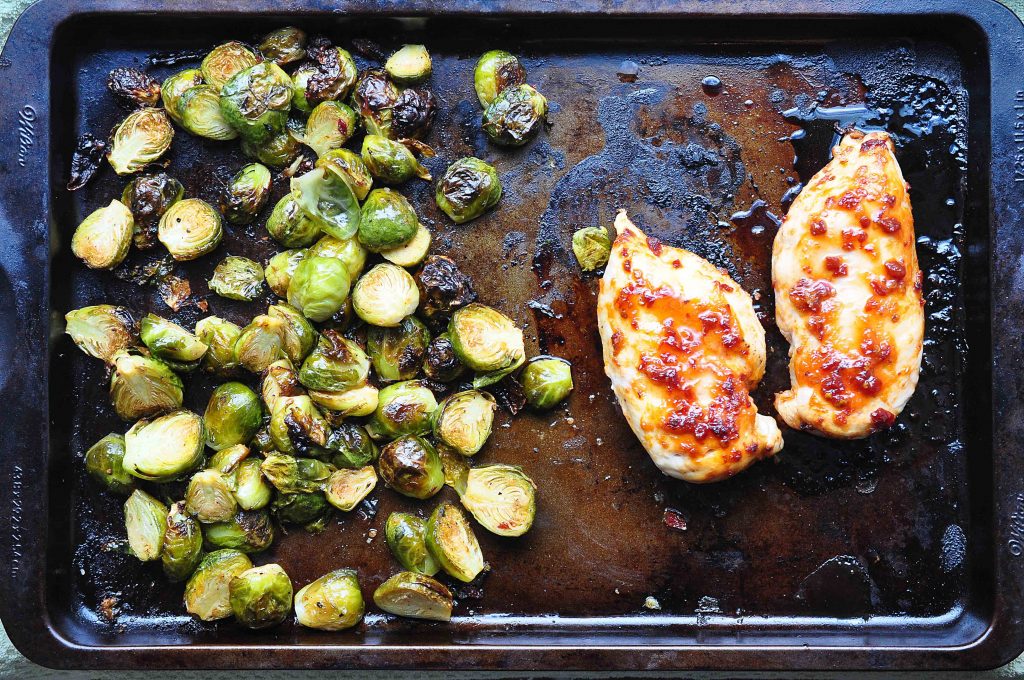 2 chipotle honey glazed chicken breasts and a pile of roasted brussels sprouts on a sheetpan