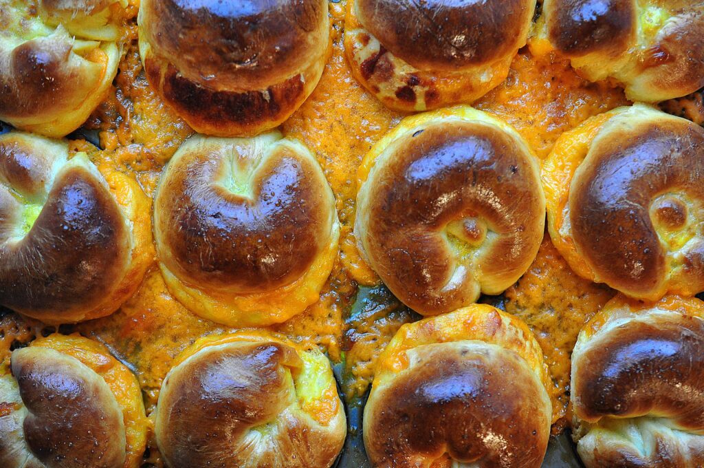 close up of tops of cheese buns in a tray with gooey cheese baked onto the pan