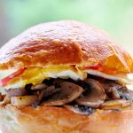 Close up of bun with fried egg, mushroom hash and a glimpse of tomato