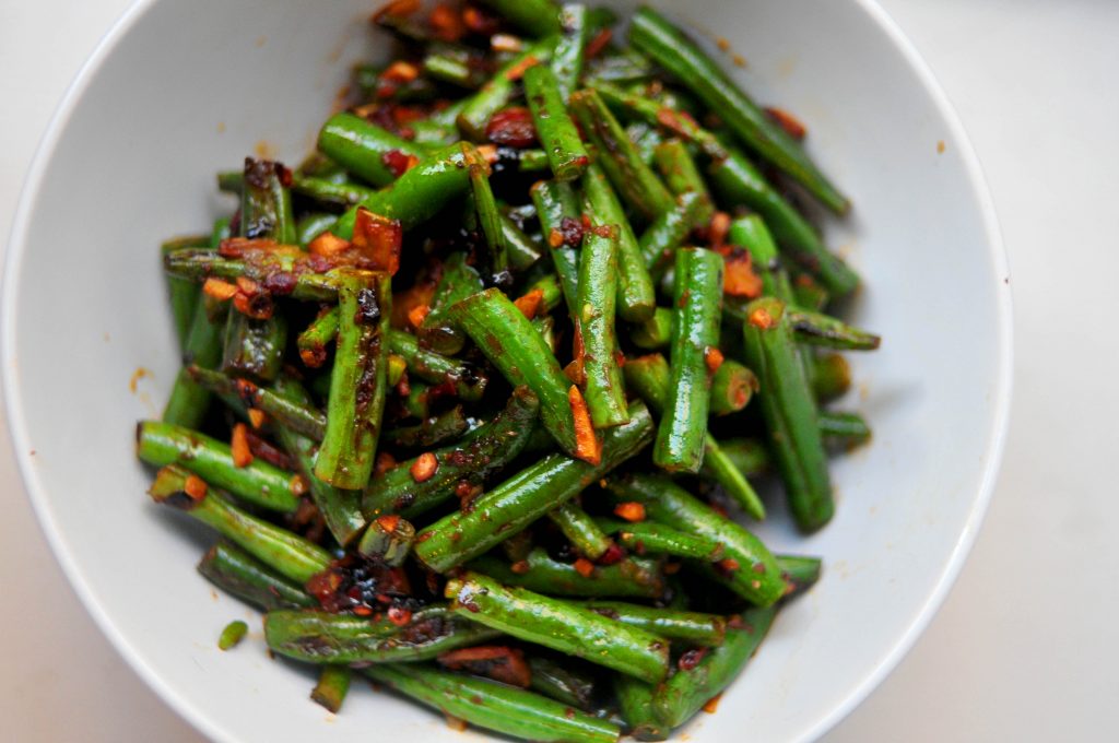 green beans covered in chile paste, garlic and soy sauce piled into a white bowl
