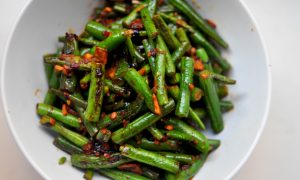 green beans covered in chile paste, garlic and soy sauce piled into a white bowl