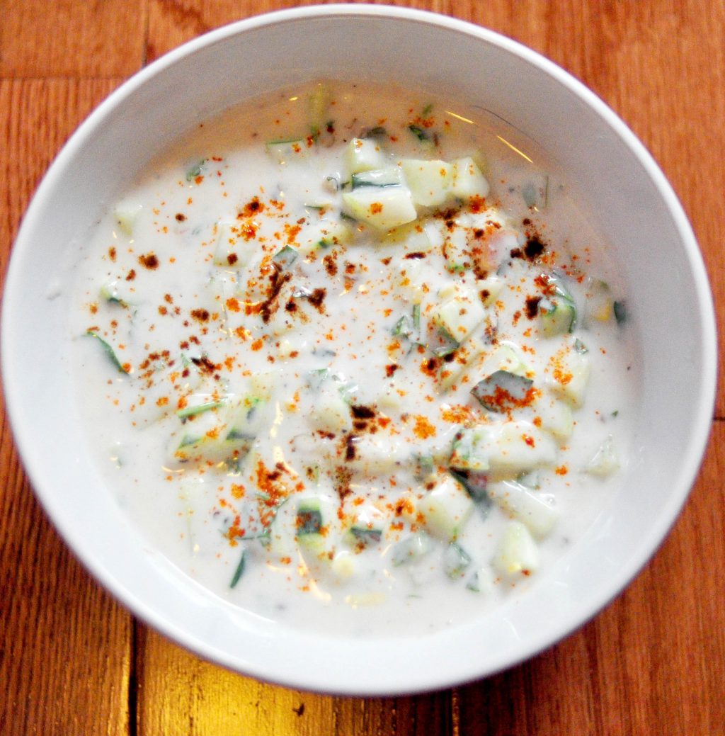white bowl filled with raita, which is yogurt with cucumber and spices