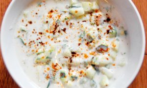white bowl filled with raita, which is yogurt with cucumber and spices