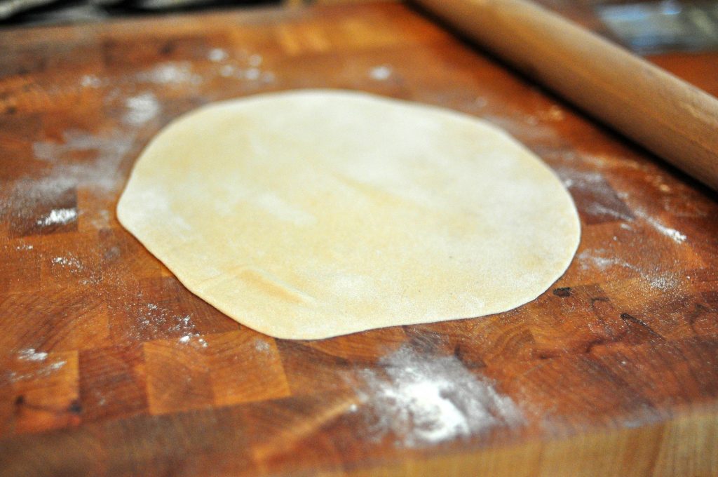 rolled out roti on a countertop with rolling pin in background