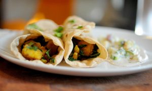 Potato and kale rolled up in a roti with raita on the side and cilantro sprinkled on top.