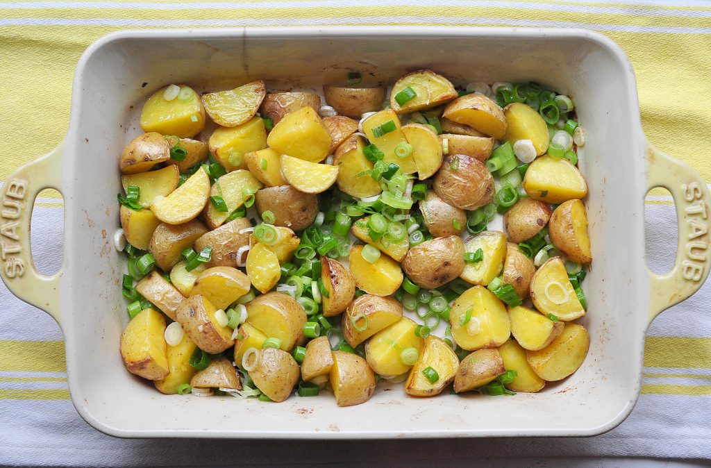 quartered roasted potatoes tossed with scallions in a casserole dish 