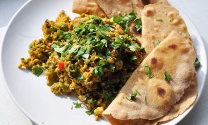 white plate with pile of very yellow scrambled eggs and vegetables with cilantro on top and four pieces of roti