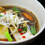 Tofu hot pot, bowl of noodles, tofu and vegetables in a warm ginger-garlic broth