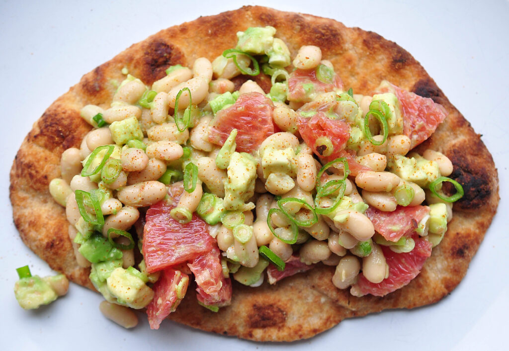 naan bread piled high with avocado, white bean and grapefruit salad