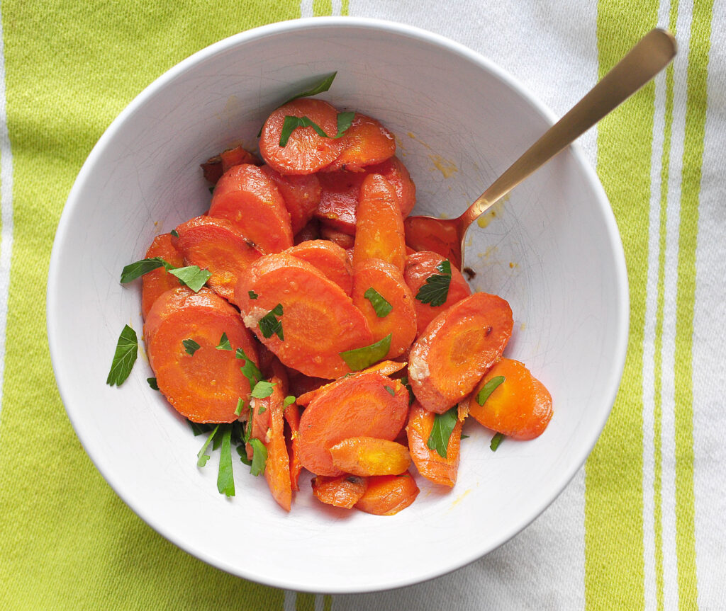 roasted sliced carrots with ginger and butter piled in a white bowl with a light green and white cloth underneath