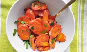 roasted sliced carrots with ginger and butter piled in a white bowl with a light green and white cloth underneath