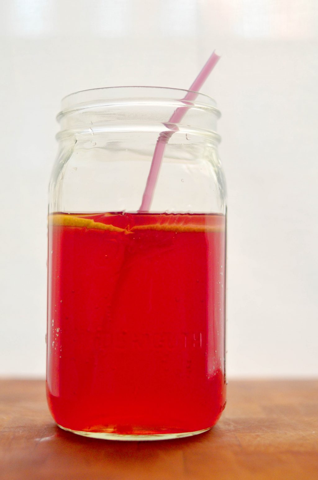 jar of bright pink agua fresca with lemon slices floating in it and a straw