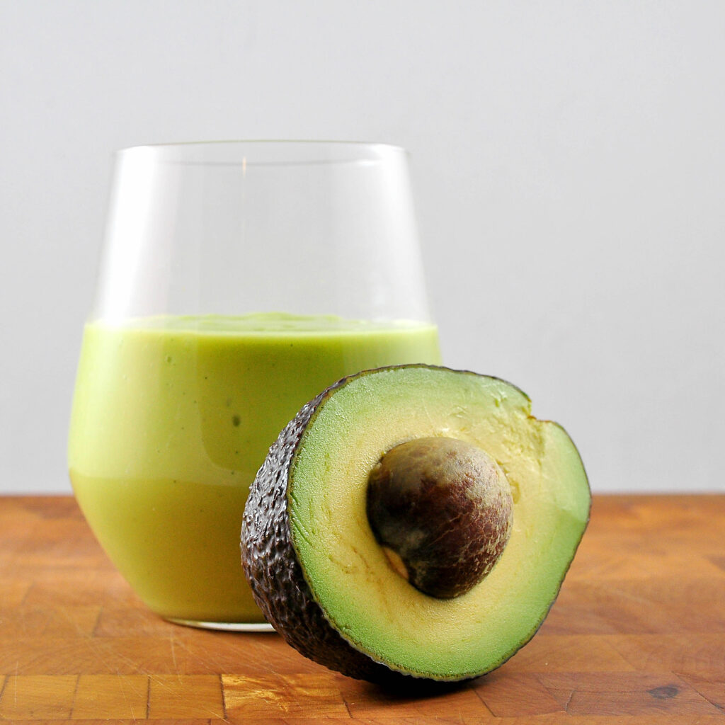 avocado milkshake in glass with half an avocado leaning on it