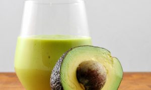 avocado milkshake in glass with half an avocado leaning on it