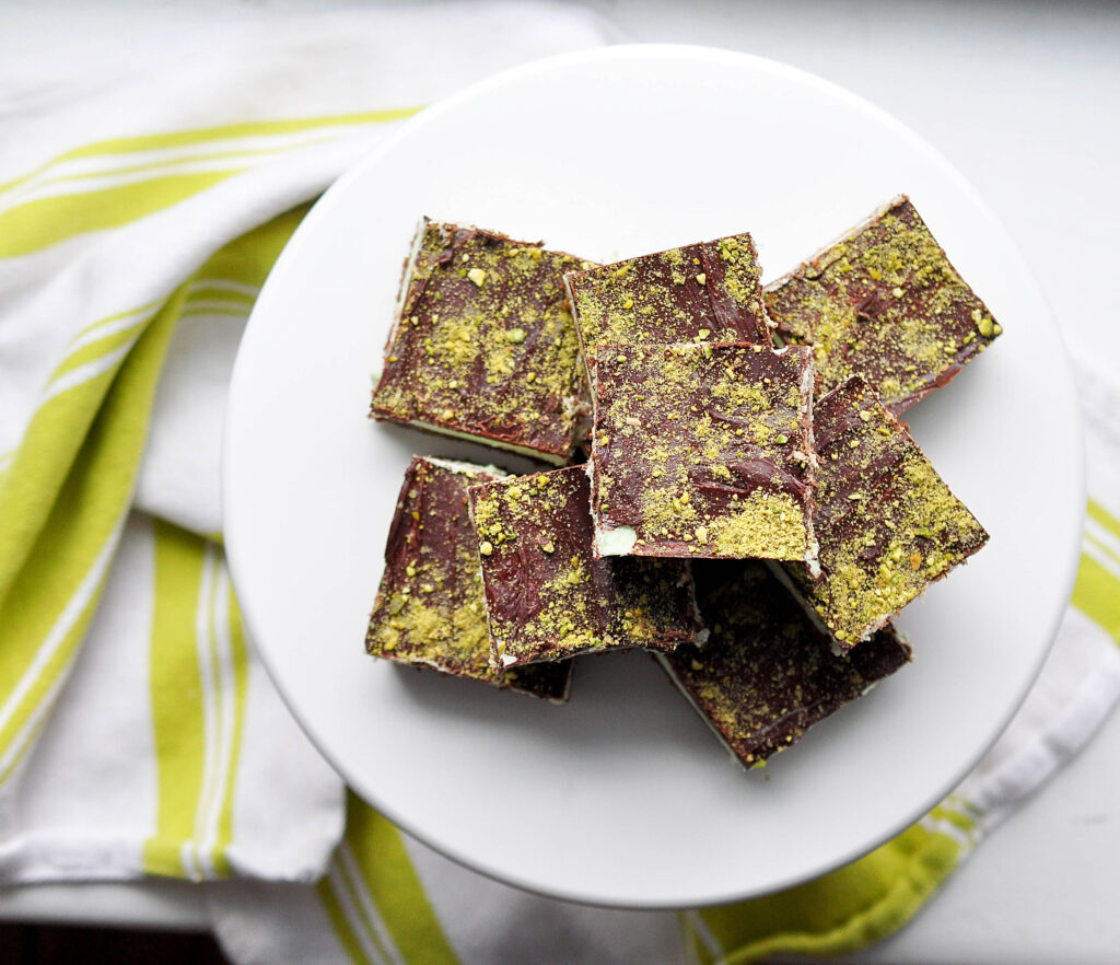 pistachio nanaimo bars from above on a white plate with a bright green striped tea towel