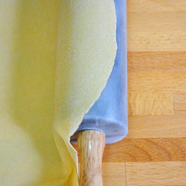 Thin piece of rolled out fresh pasta dough draped over a rolling pin
