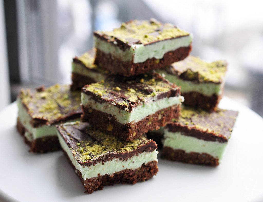 pistachio nanaimo bars on a white tray in a pile