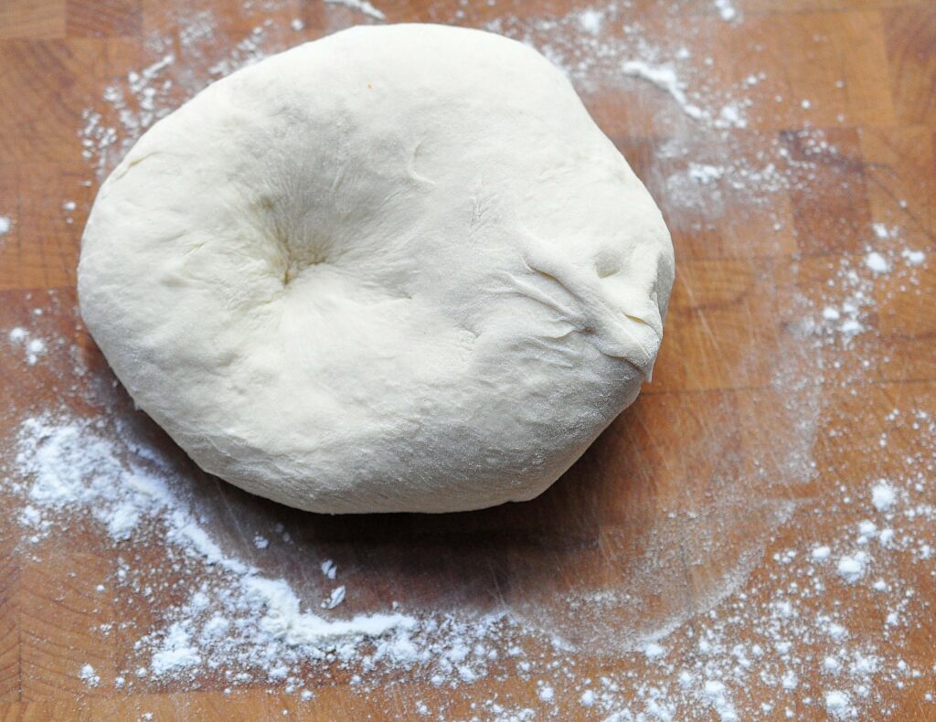 raw pizza dough on a wooden board with flour sprinkled around