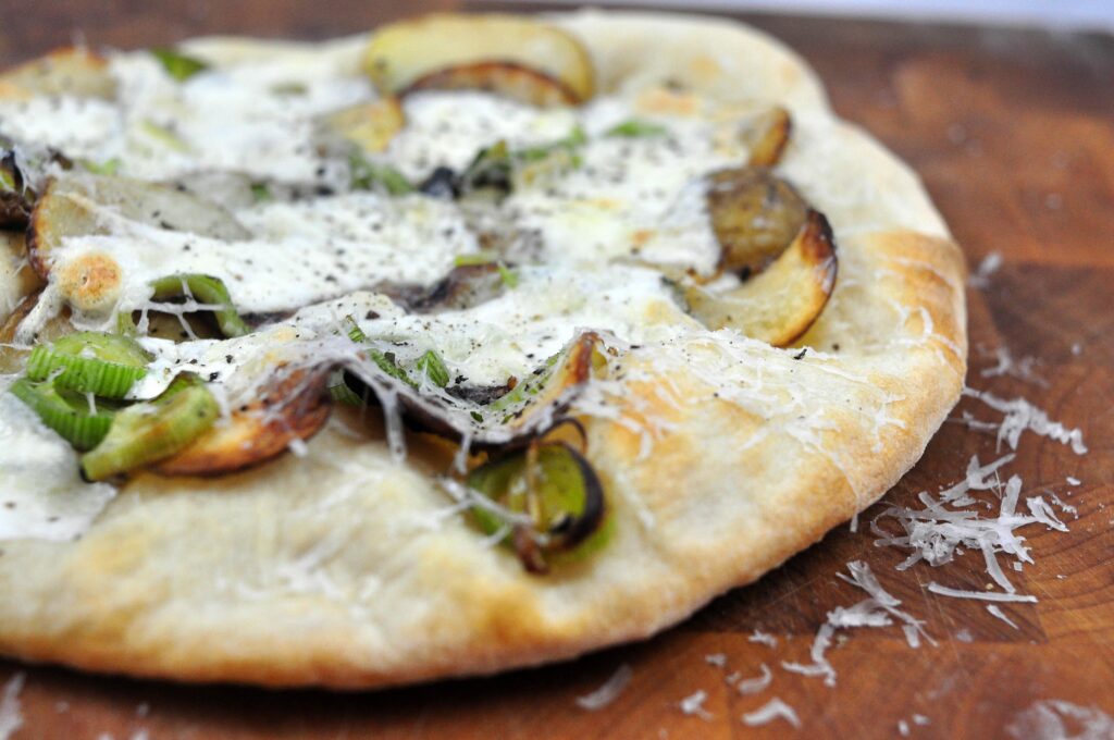 side view of potato and leek pizza on a wooden board