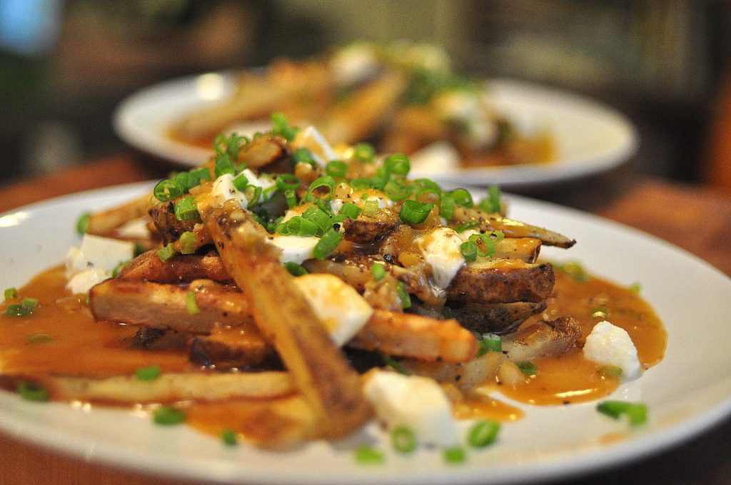 poutine! oven baked fries smothered in gravy, mozzarella and scallions on a white plate