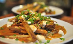 poutine! oven baked fries smothered in gravy, mozzarella and scallions on a white plate