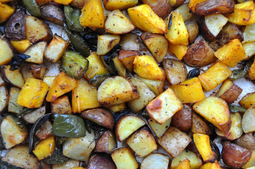 an expanse of roasted vegetables including potatoes, swee potatoes, peppers and squash