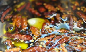 close up of chiles, garlic and spices infusing into oil