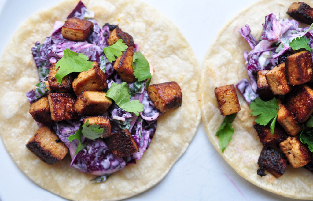 two tofu and peanut cabbage slaw tacos on a white background