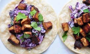 two tofu and peanut cabbage slaw tacos on a white background